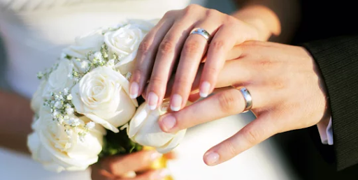 A couple showing their wedding ring holding a white Rose Bouquet image.